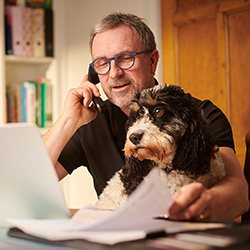 Man working at home on computer, with dog on his lap